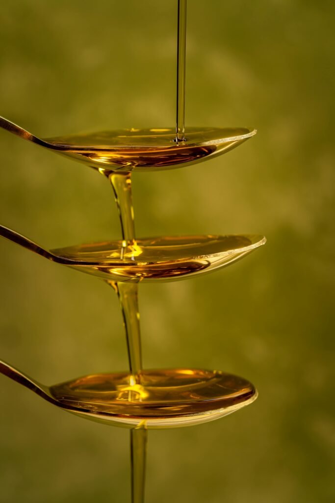 Artistic capture of honey pouring over stacked spoons with a green background.